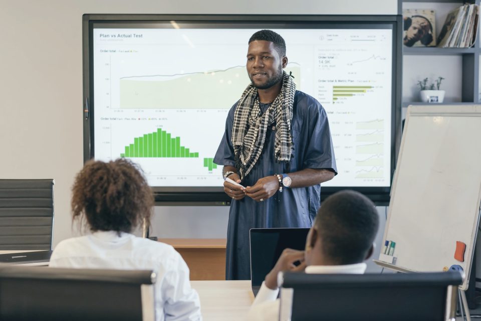 A man presenting charts on a large screen to colleagues in a meeting room